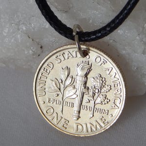 May include: A silver dime coin pendant with a black cord necklace. The coin features a torch, olive branch, and oak branch design. The words "UNITED STATES OF AMERICA" and "ONE DIME" are visible.