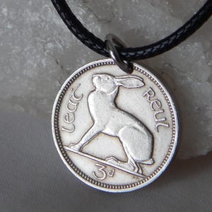 May include: A silver coin pendant necklace with a hare design. The coin has the words "Lear" and "Reul" around the edge, and the number "3d". The pendant is suspended from a black cord.
