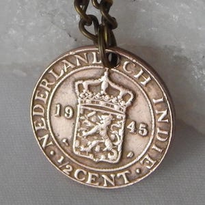 May include: A copper-coloured coin pendant from the Netherlands Indies. The coin shows a crown, a lion, and the text "NEDERLANDSCH INDIE" and "1/2 CENT" with the year 1945.