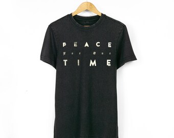 Könnte beinhalten: Dunkelgraues T-Shirt mit den Worten "PEACE for our TIME" in weißen Blockbuchstaben aufgedruckt. Das Shirt hängt an einem Holzbügel vor weißem Hintergrund. Das T-Shirt hat kurze Ärmel und einen Rundhalsausschnitt.