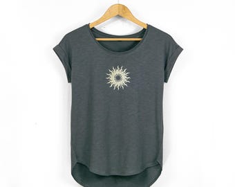May include: Dark gray t-shirt with a crew neck and rolled sleeves, hanging on a wooden hanger. A cream-colored sunburst design is centered on the chest. The shirt has a curved hemline.