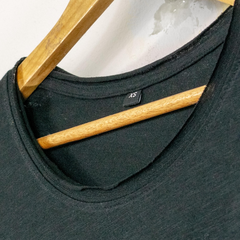 Close-up of scoop neckline on black womens t shirt, soft wide neck with clean stitching and lightweight raw-cut cotton fabric.