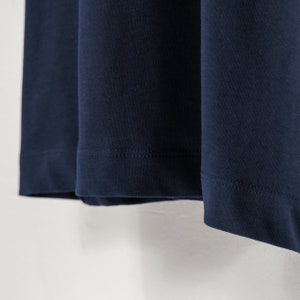 May include: Close-up of the bottom hem of a navy blue long-sleeved shirt. The hem is sewn with a straight stitch.