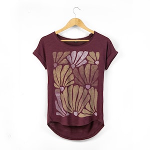 May include: Burgundy t-shirt with a floral design. The short-sleeved shirt features a scoop neck and a curved hemline. The floral pattern is composed of gold and lavender-coloured stylized flowers.