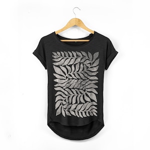 May include: Black t-shirt with a grey leaf pattern. The short-sleeved shirt is hanging on a wooden hanger against a white background. The leaf design is a repeating pattern of stylized leaves.