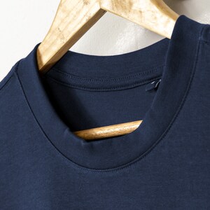 May include: A navy blue t-shirt with a ribbed crew neck collar. The shirt is hanging on a wooden hanger.