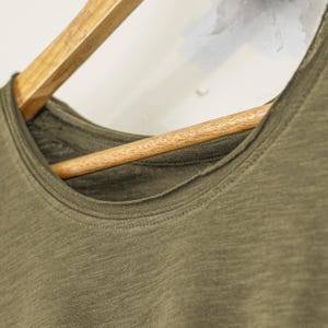 Detailed view of scoop neckline and inner stitching on a women’s olive slub cotton t-shirt. The raw edge detailing adds character to this soft, relaxed-fit tee, ideal for layering in minimalist, spiritual, or boho-inspired outfits. The breathable texture of the fabric and simple styling reflect a calm, natural aesthetic.