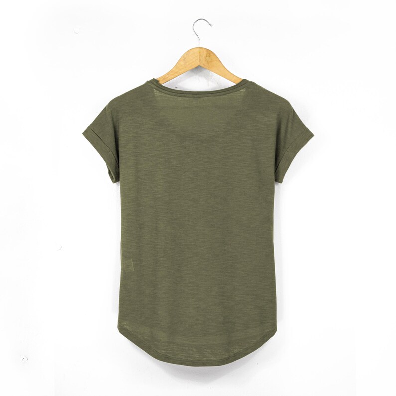 Rear view of olive green women’s t-shirt made from breathable slub cotton, displayed on a wooden hanger. The scoop neck and rolled sleeves offer a relaxed, feminine fit, while the dropped hem provides a flattering silhouette. This sustainable casual top is ideal for layering in a laid-back boho or earthy wardrobe.