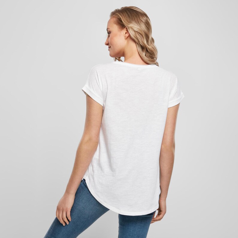 Rear model view showing the soft drape of the white scoop neck t shirt with rolled sleeves and longer curved back hem.