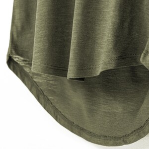 Detailed shot of the dropped hemline on a women’s olive slub cotton t-shirt, highlighting the light texture of the fabric. The gently curved back hem adds flow and shape, complementing the relaxed, scoop neck cut. This comfortable style is designed with a subtle slub weave, making it breathable and ideal for a casual look.