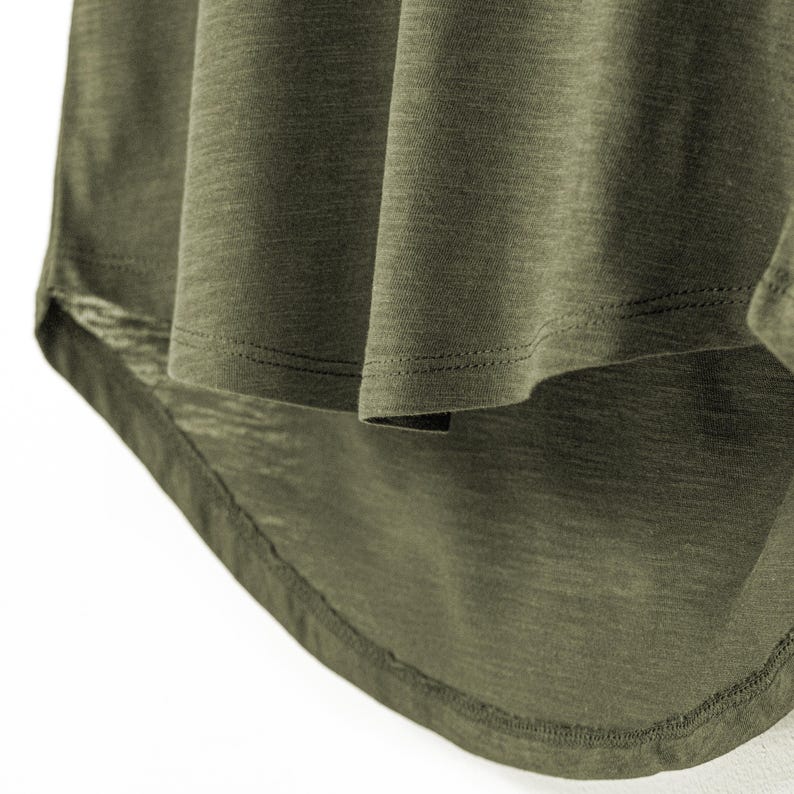 Detailed shot of the dropped hemline on a women’s olive slub cotton t-shirt, highlighting the light texture of the fabric. The gently curved back hem adds flow and shape, complementing the relaxed, scoop neck cut. This comfortable style is designed with a subtle slub weave, making it breathable and ideal for a casual look.