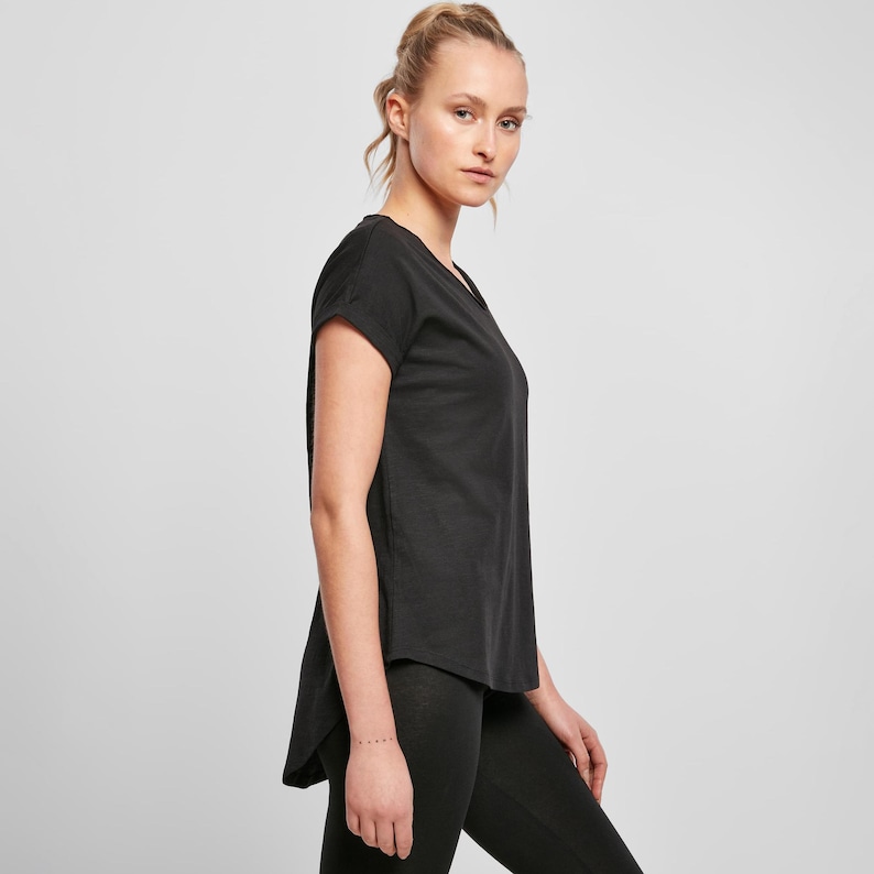 Woman wearing black relaxed fit t shirt side view, showing loose drape and curved hem, paired with leggings for casual everyday outfit