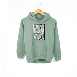 Könnte beinhalten: Ein salbeigrüner Hoodie mit einer schwarz-weißen Comic-Grafik eines Roboters, der eine Stadt angreift. Die Grafik lautet "Robot Attack!"
