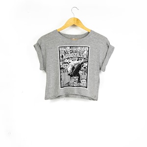 May include: A grey cropped t-shirt featuring a black and white graphic print of a Godzilla comic book cover. The text on the cover reads "Vintage Comic Book Edition The Return of Godzilla".
