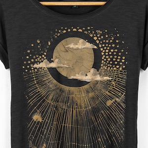 Close up of celestial moon graphic on black t shirt showing detailed clouds, circular moon design and radiating lines in a soft distressed gold print