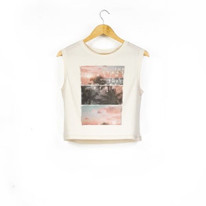May include: A white sleeveless crop top with a graphic print of a sunset and palm trees. The text "THE STARS ALIGN THEY DO NOT BIND US" is printed on the graphic.