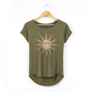 Olive relaxed-fit women’s T-shirt with scoop neck, rolled sleeves and curved back hem, shown on a wooden hanger against a white wall, featuring a centred vintage sun face print in soft tan.