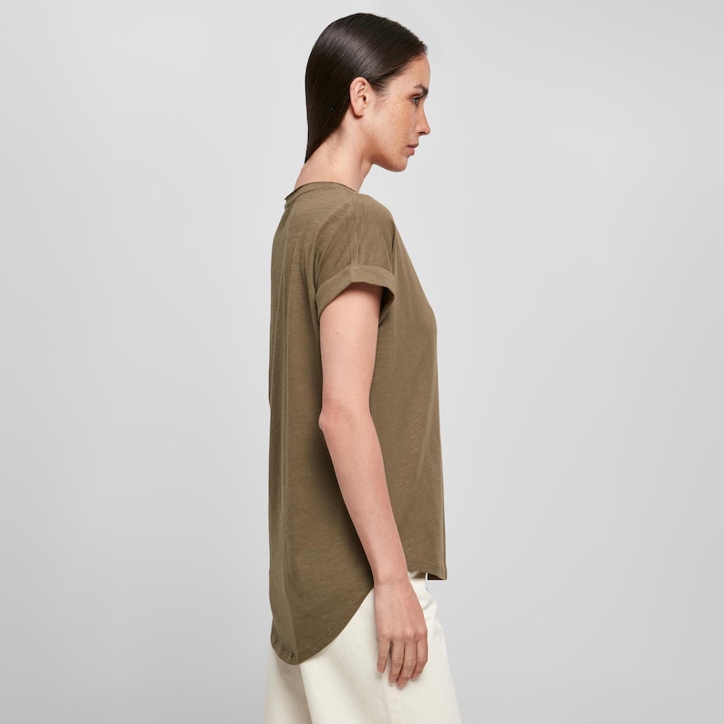 Side profile of model wearing women’s slub cotton scoop neck t-shirt in olive green. The relaxed fit drapes naturally with a curved back hem and rolled sleeves, ideal for casual styling. Lightweight, breathable, and subtly spiritual, this t-shirt suits everyday wear for boho wardrobes.