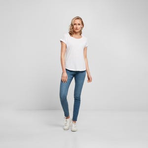 Full body model image showing the white scoop neck t shirt styled with slim fit denim and white trainers, highlighting the relaxed casual silhouette.