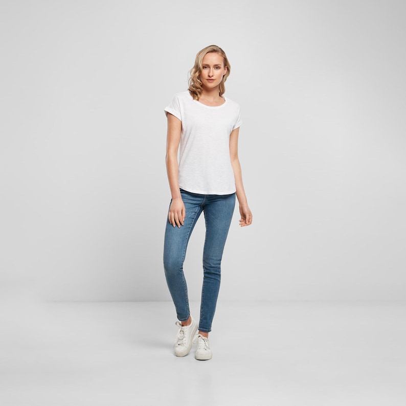 Full body model image showing the white scoop neck t shirt styled with slim fit denim and white trainers, highlighting the relaxed casual silhouette.