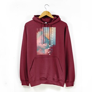 Può includere: Una felpa con cappuccio color bordeaux con una stampa grafica di un tramonto con nuvole e il testo "FULL OF SUNSHINE" in orientamento verticale.