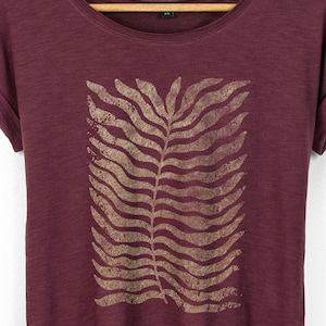 Close-up of botanical fern print on cherry red t-shirt, showing organic flowing leaf pattern with a lightly textured finish that blends into the fabric.