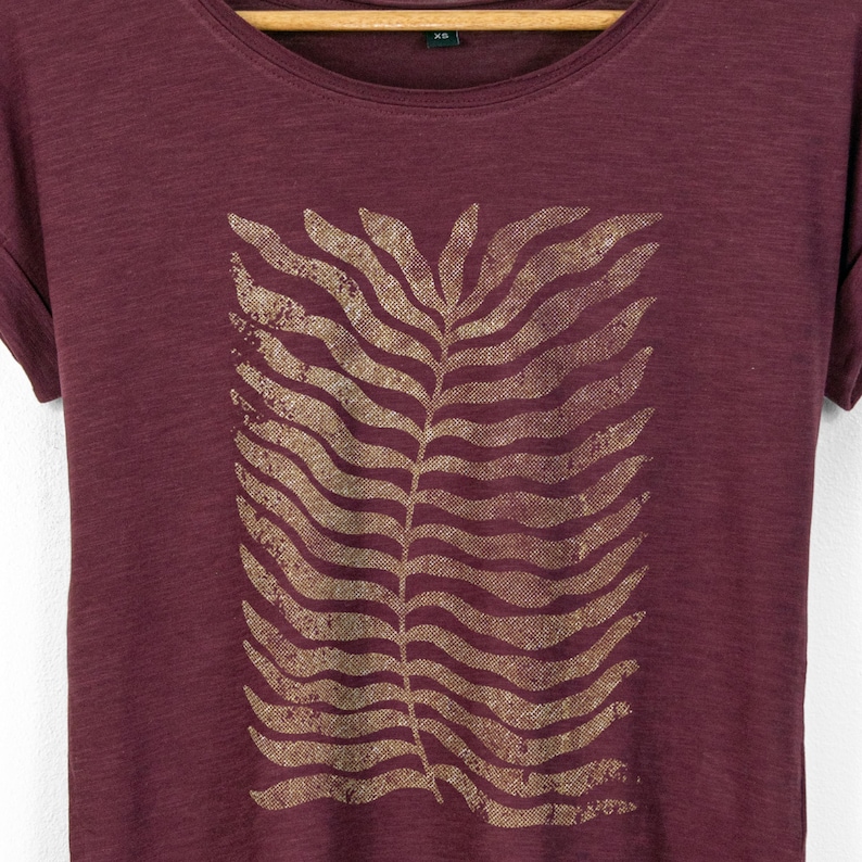 Close-up of botanical fern print on cherry red t-shirt, showing organic flowing leaf pattern with a lightly textured finish that blends into the fabric.