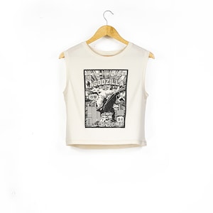 May include: A white sleeveless crop top featuring a black and white graphic print of a Godzilla comic book cover. The text on the cover reads "The Return of Godzilla".