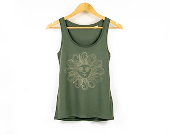 Op de afbeelding: Olijfgroene tanktop met een gouden zonnegrafiek. Het zonontwerp heeft een lachend gezicht met wervelende stralen. De mouwloze top hangt aan een houten hanger tegen een witte achtergrond. Een casual, comfortabele top.