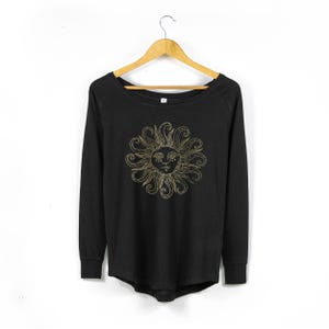 May include: Black long-sleeved shirt with a gold sun graphic. The sun has a face with closed eyes.