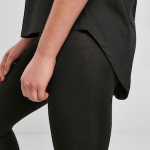 Black womens relaxed fit t shirt worn with leggings, close-up side detail showing curved hem and soft drape, lightweight cotton fabric with smooth texture, casual everyday outfit styling with clean minimal look