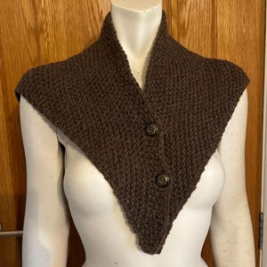 Puede incluir: Un cuello de punto marrón con dos botones. El cuello está en un maniquí blanco.