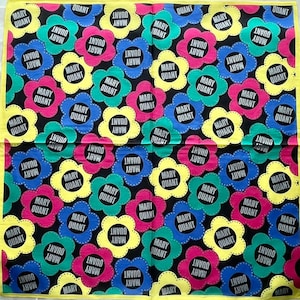 Könnte beinhalten: Ein schwarz-weiß gemustertes Bandana mit einem sich wiederholenden Muster aus stilisierten Blumen. Die Blumen sind in den Farben Rosa, Gelb, Blau und Grün gehalten. Der Text "MARY QUANT" wird im gesamten Design wiederholt.