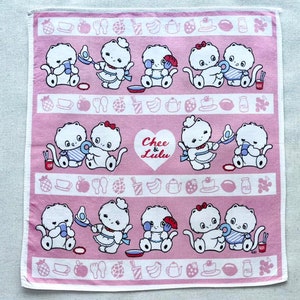 May include: A pink and white cotton tea towel with a repeating pattern of cartoon cats and kitchen items. The text "Chee & Lulu" is in a heart shape in the centre of the towel.