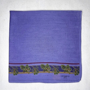 Peut inclure: Un mouchoir carré lavande avec un motif subtil de points. La bordure inférieure présente une bande décorative avec des motifs cachemire verts, dorés et violets, avec le texte "ungaro paris".