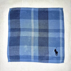May include: Blue plaid handkerchief with a dark blue embroidered logo of a person on a horse. The handkerchief features a classic plaid pattern in shades of blue.