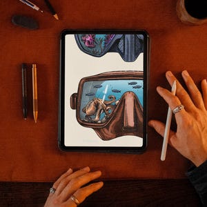 K&ouml;nnte beinhalten: Ein digitales Tablet zeigt eine detaillierte Illustration einer braunen Tauchmaske. Im Inneren des Maskenglases schwimmt ein kleiner Oktopus zwischen winzigen blauen Fischen. Die Illustration hat einen hellen cremefarbenen Hintergrund.