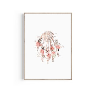 Pode incluir: Uma ilustração em aquarela de um esqueleto de mão humana cercado por rosas cor-de-rosa e pêssego. Os ossos são representados em cobre.