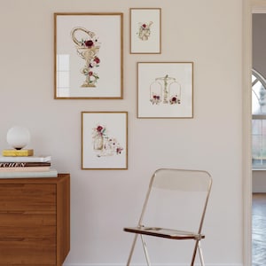 Puede incluir: Cuatro impresiones de acuarela enmarcadas con acentos dorados y dise&ntilde;os florales. Las impresiones presentan una serpiente envuelta alrededor de una copa, una balanza, un frasco con flores y una calavera con flores.