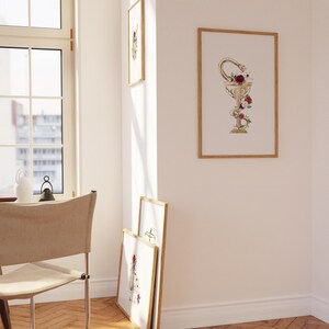 Puede incluir: Tres impresiones enmarcadas en una pared blanca. La impresi&oacute;n central presenta un c&aacute;liz dorado con una serpiente enroscada alrededor y flores rojas y blancas. Las otras dos impresiones est&aacute;n desenfocadas.
