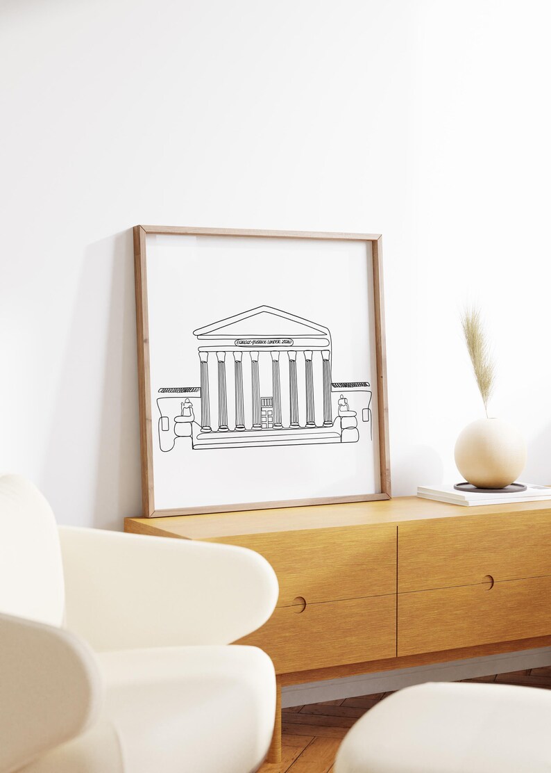 May include: A black and white line drawing of the Supreme Court building in Washington, D.C. The drawing is framed in a light wood frame and is hanging on a white wall.