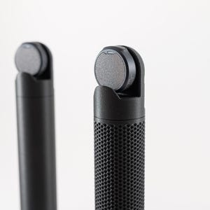May include: Two black, cylindrical objects with a textured grip and a circular top. One object has a smooth surface, while the other has a perforated pattern. The tops are gray and circular, and the background is white.