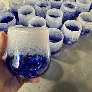 May include: A collection of stemless drinking glasses with a unique design. The glasses feature a white and blue speckled pattern, with a deep blue base. The glasses are made of glass and are suitable for various beverages.