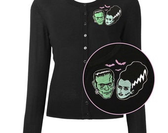 May include: Black cardigan with a green and pink embroidered design of Frankenstein and his bride. The design includes bats flying above them.