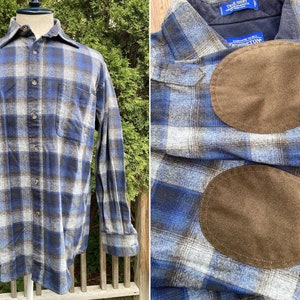 Può includere: Camicia di flanella a quadri blu e grigia con toppe in pelle scamosciata marrone sui gomiti. La camicia ha un colletto abbottonato e maniche lunghe.