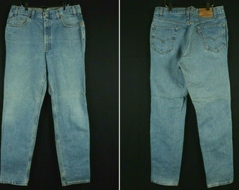 May include: A pair of light blue denim jeans with a classic straight leg fit. The jeans have a button fly and five pockets. The back pockets have a red leather patch with the Levi's logo.