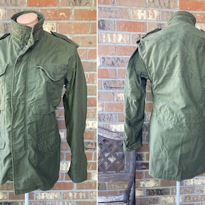 May include: A green military-style jacket with a button-up front, two large pockets, and a drawstring waist.