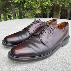 Puede incluir: Un par de zapatos de vestir de cuero burdeos oscuro con cordones negros. Los zapatos tienen un diseño clásico con punta redonda y suela negra gruesa. Los zapatos están en buen estado y parecen estar bien cuidados.