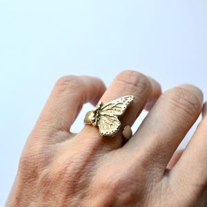 May include: A gold-toned ring featuring a detailed butterfly design. The butterfly is textured and has a three-dimensional appearance.