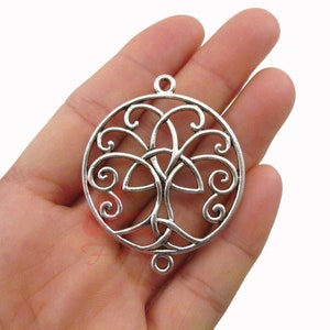 May include: Silver-toned metal pendant featuring a Celtic tree of life design. The pendant is circular with intricate swirling patterns and a central tree motif. It has a loop at the top and bottom for attachment, suitable for jewelry making or crafting.